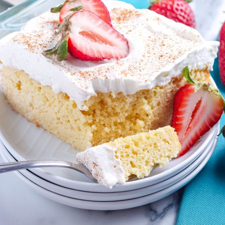 A close up picture of a slice of Tres Leches Cake on a white plate garnished with strawberries.