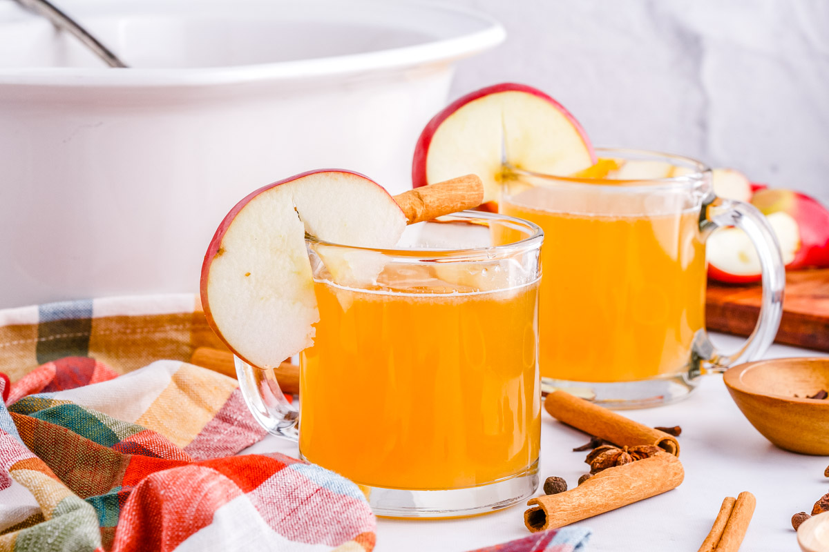 Two mugs of slow cooker apple cider with a slow Coker in the background.