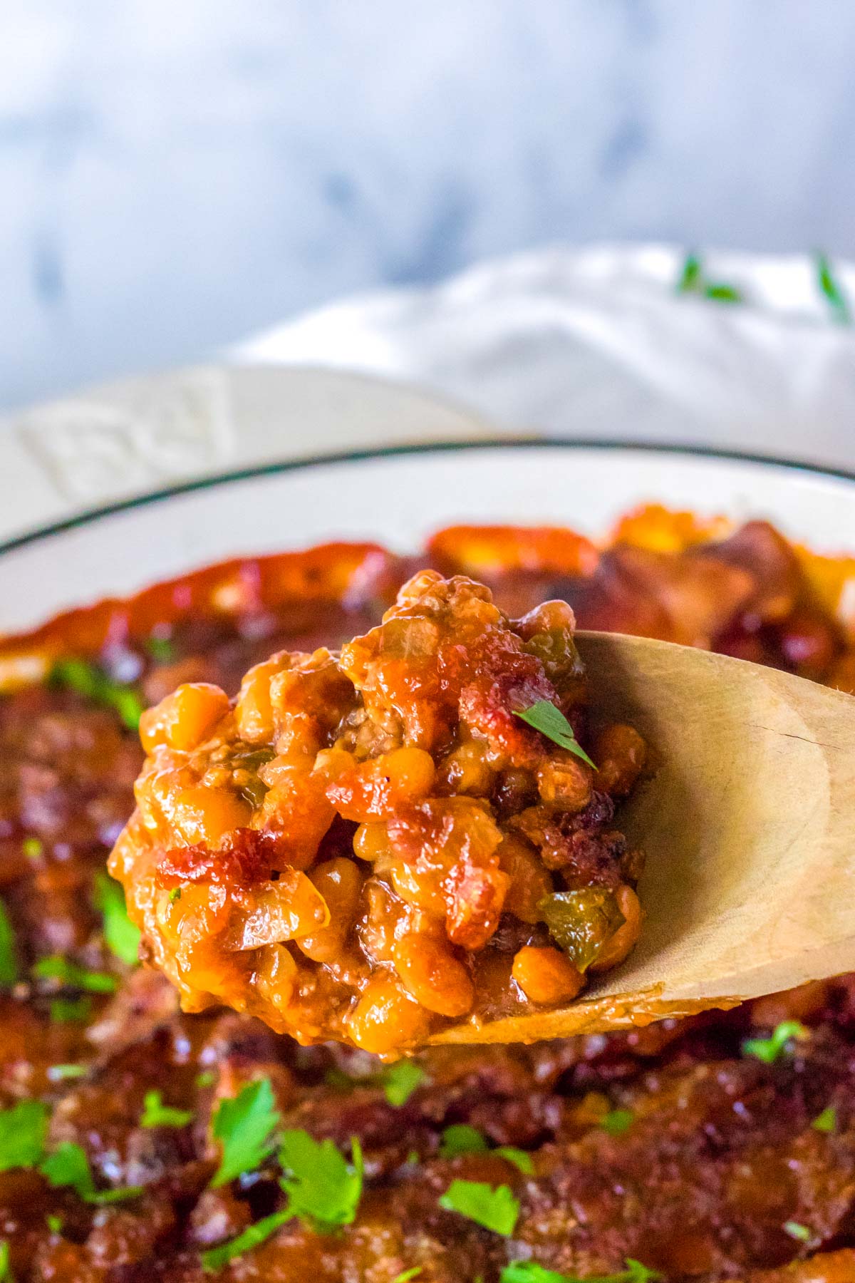 A wooden spoon picking up some of the finished beefy baked beans.