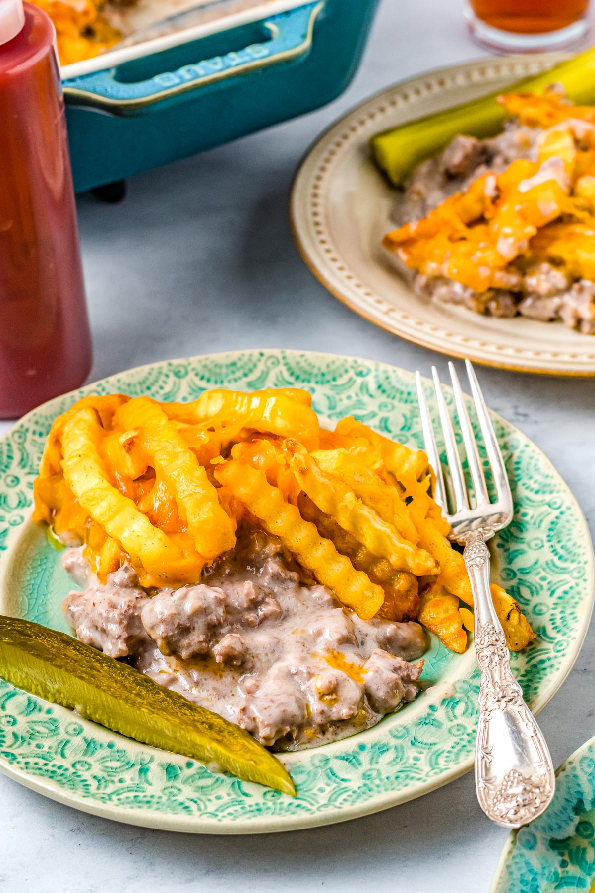 Some of the Cheeseburger Casserole with French Fries on a plate with a pickle spear and some ketchup.