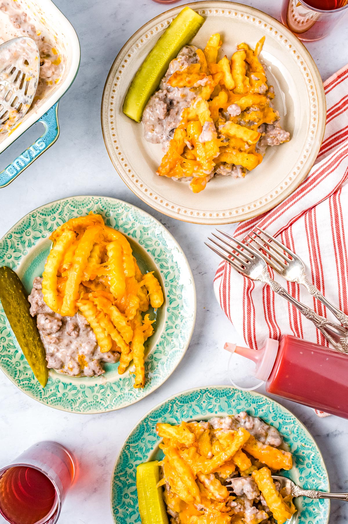 An overhead picture of plates with some of the Cheeseburger French Fry Casserole recipe on them and pickle spears.