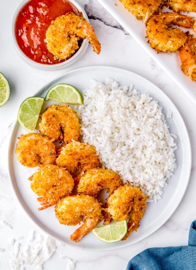 An overhead picture of the finished Coconut Shrimp on a plate with white rice and lime wedges.