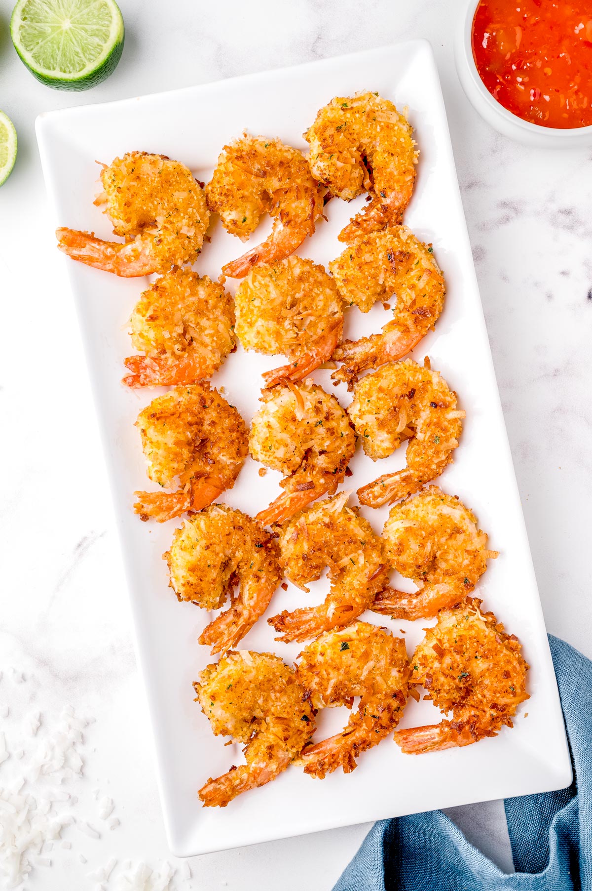 Th finished Coconut Shrimp recipe on a white platter with some mango sauce and limes nearby.