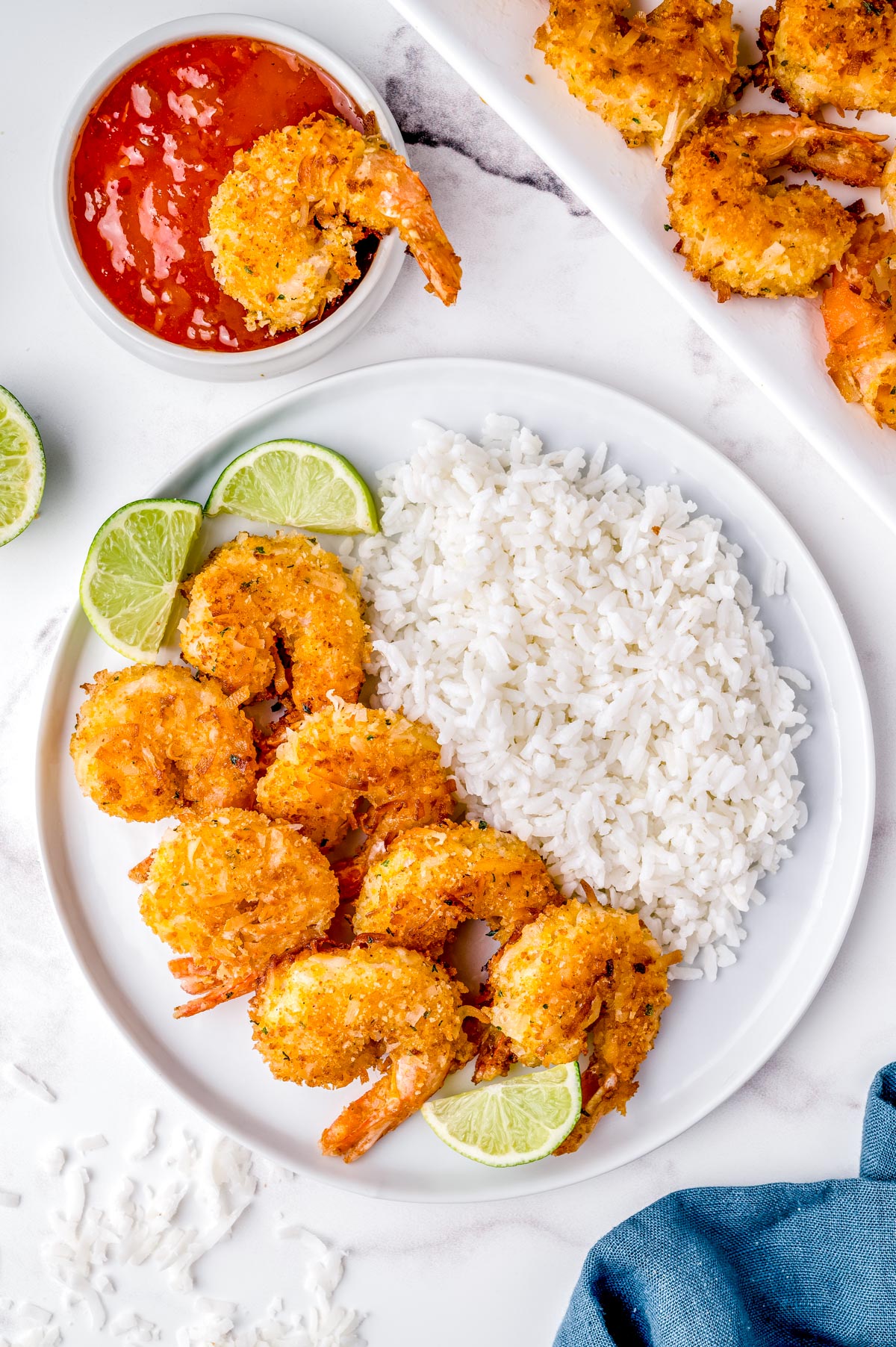 An overhead picture of the finished Coconut Shrimp on a plate with white rice and lime wedges.