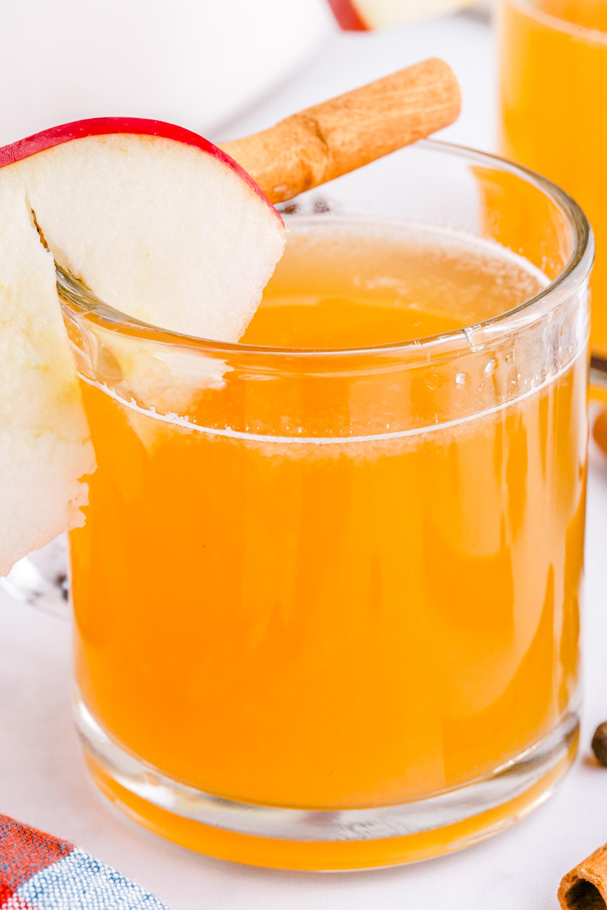 A close up picture of the finished crockpot apple cider in a glass mug garnished with an apple slice and cinnamon stick.