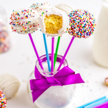 The finished Donut Hole Cake pops standing upright in a glass jar, one with a bite taken out of it.
