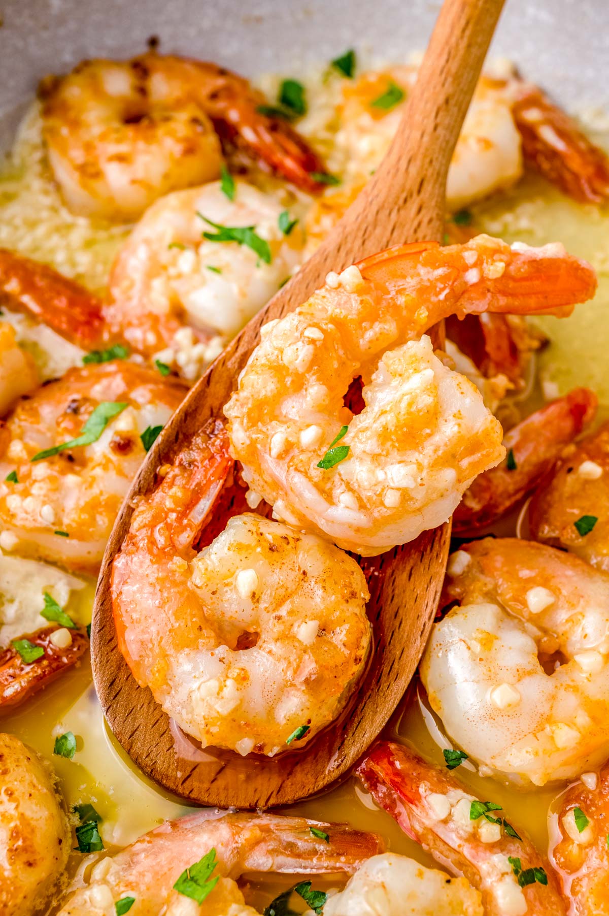 A wooden spoon picking up some of the Hawaiian garlic shrimp from the pan they were cooked in.