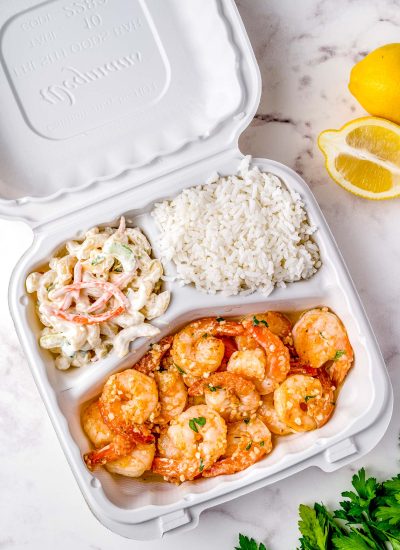 The finished Hawaiian Garlic Shrimp in a take out container with white rice and macaroni salad.