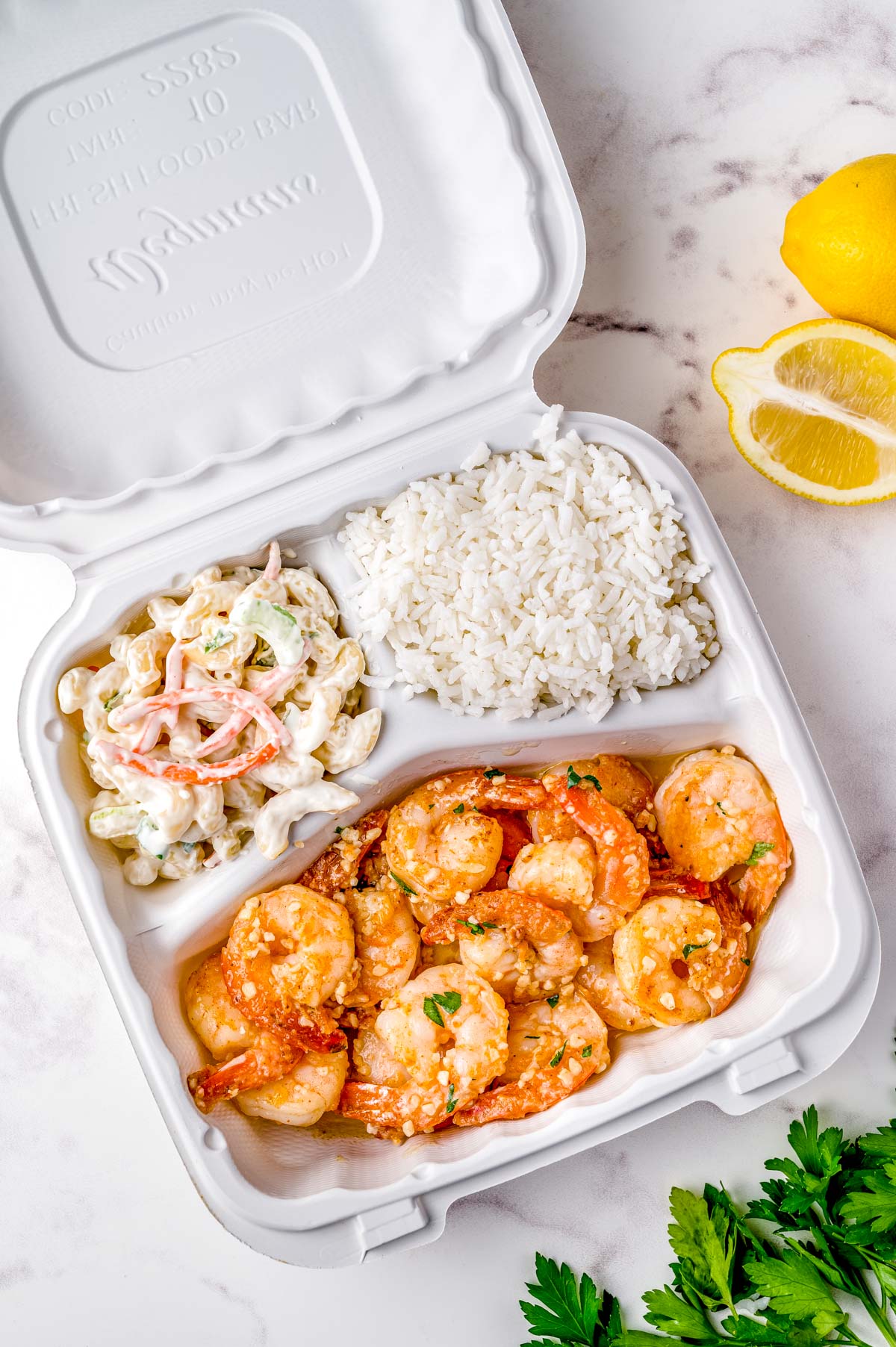 The finished Hawaiian Garlic Shrimp in a take out container with white rice and macaroni salad.