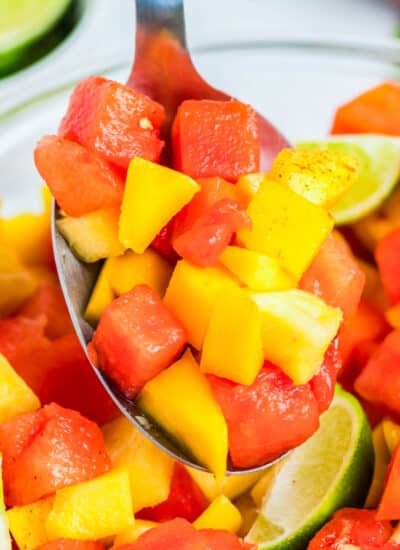 A spoon picking up some Mexican Fruit Salad from a serving bowl.