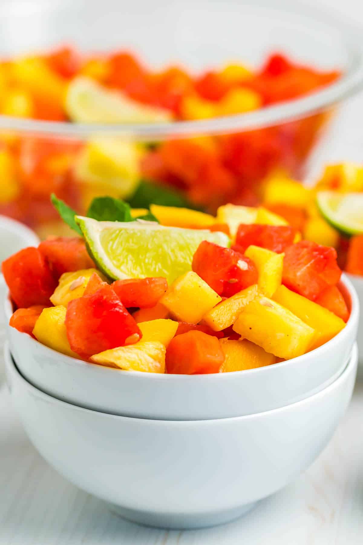 Fruit salad in a white bowl garnished with a lime wedge.