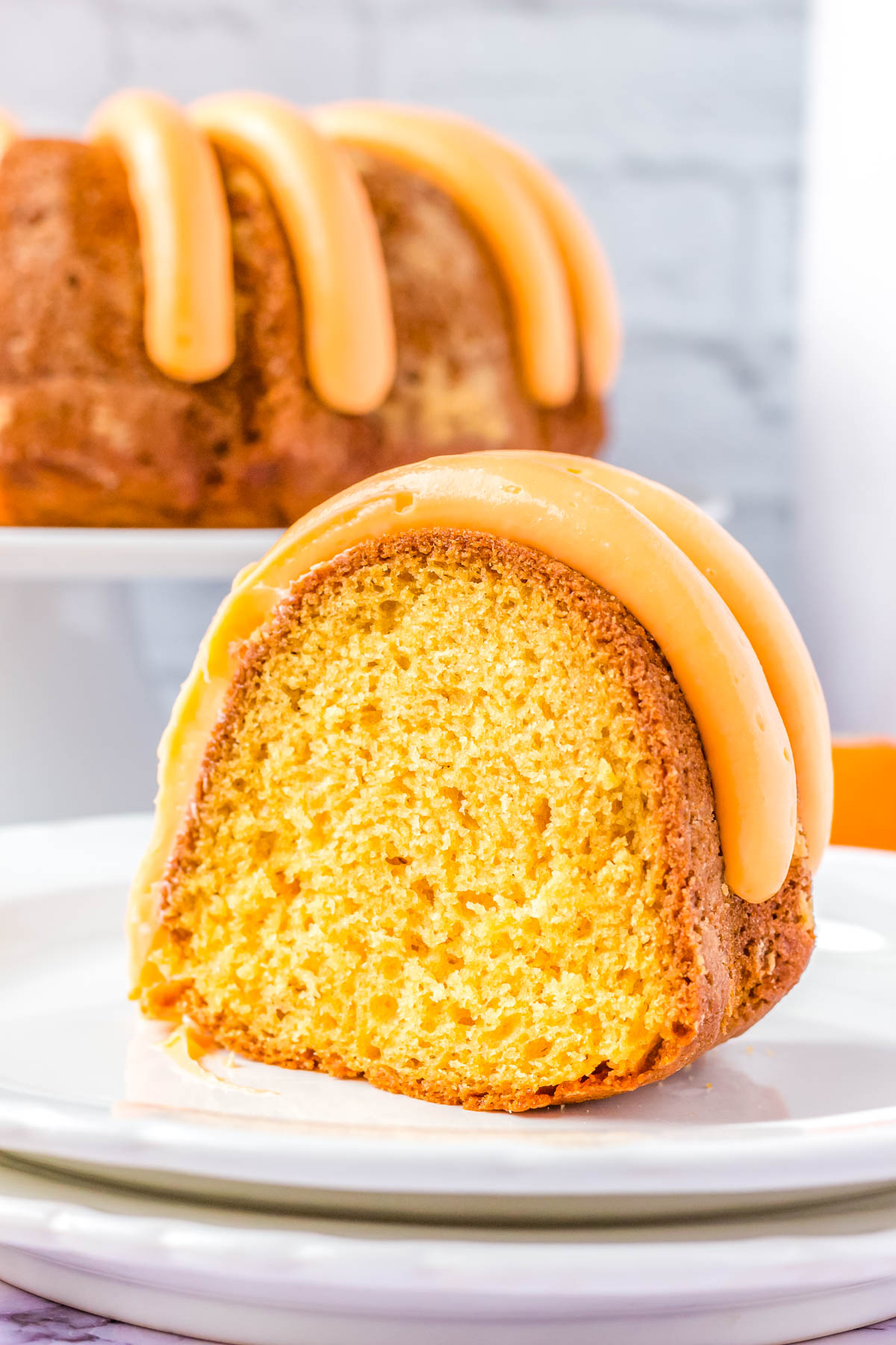 A slice of the Orange Bundt Cake on a white slate with frosting on it.