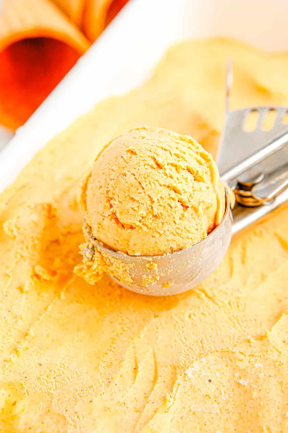 An ice cream scoop scooping up some of the finished pumpkin ice cream from the container.