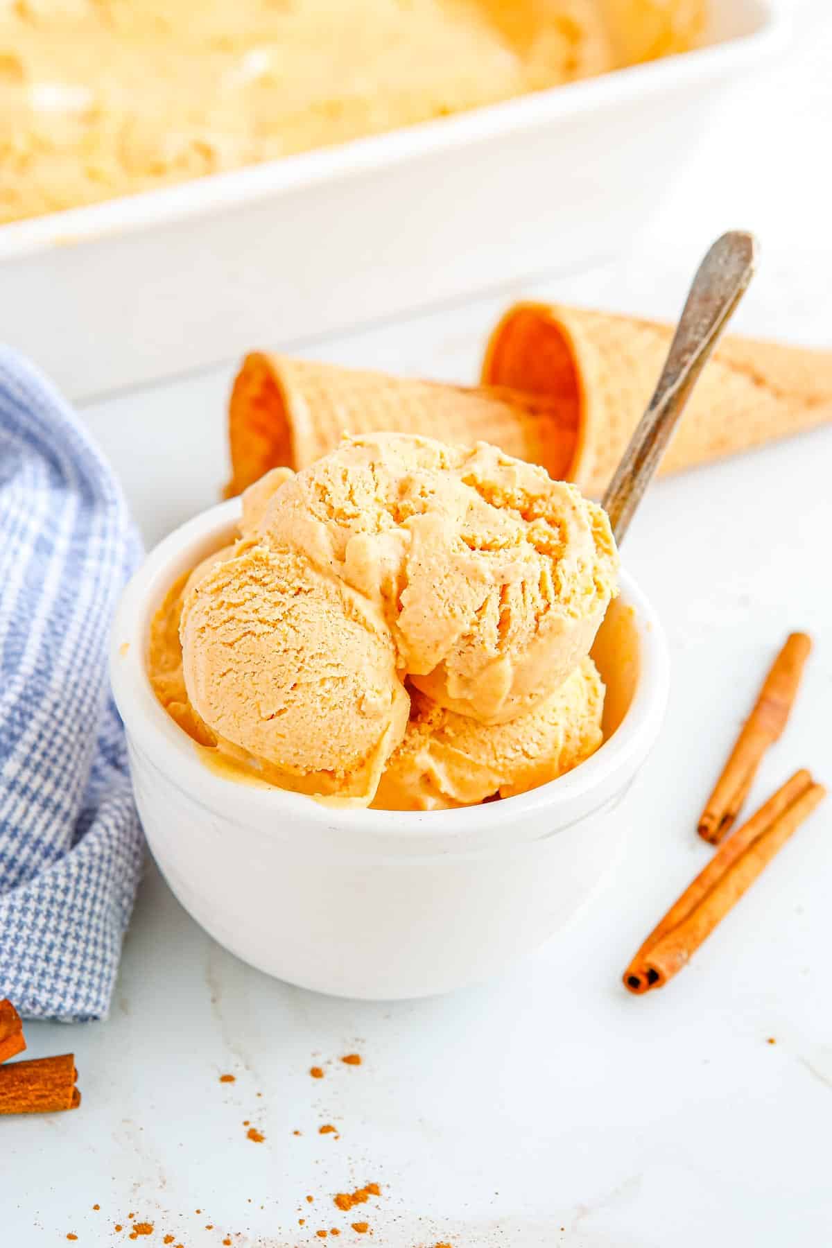 The finished Pumpkin Pie Ice Cream in a white bowl with ice cream cones in the background.