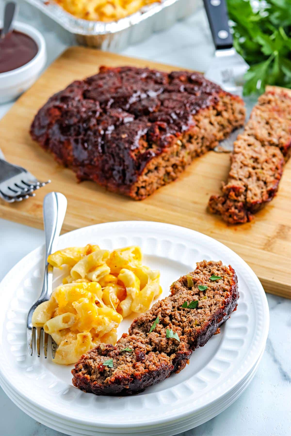 A close of the finished smoked meatloaf on a white plate with Mac and cheese.