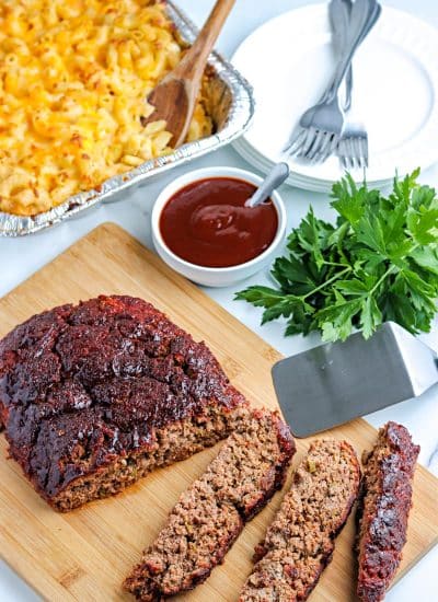 The finished smoked meatloaf on a cutting board with smoked Mac and cheese in the background.