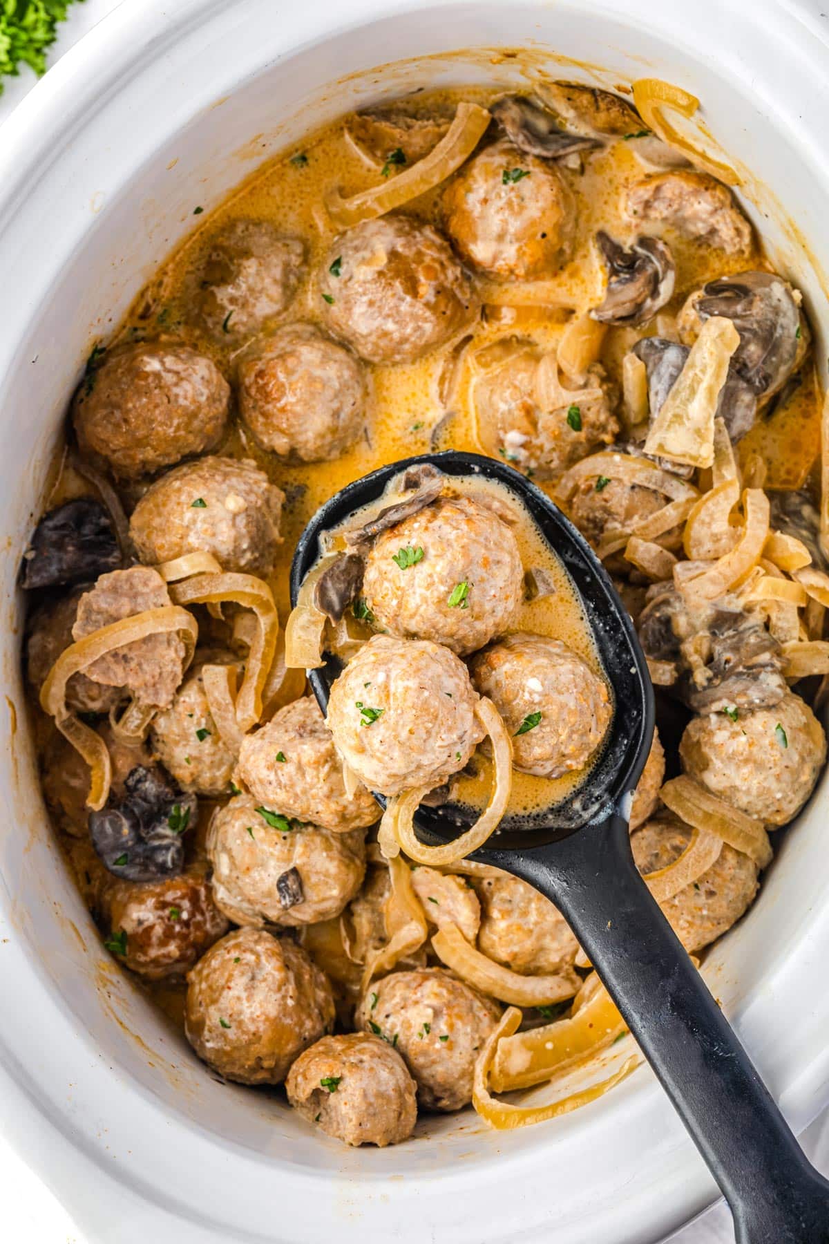 A serving spoon picking up some of the finished Beef Stroganoff Meatballs from the slow cooker.