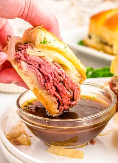 One of the finished French Dip Sliders being dipped into a bowl of au jus.