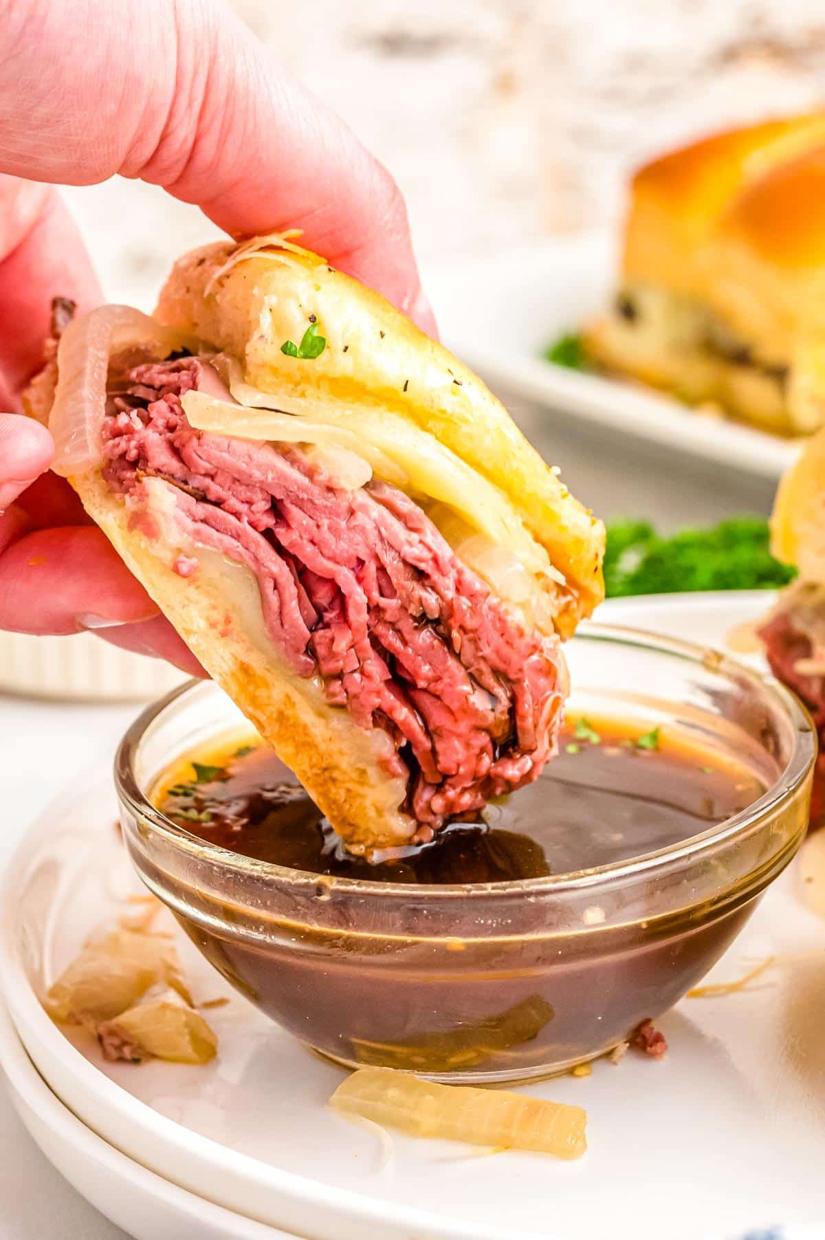 One of the finished French Dip Sliders being dipped into a bowl of au jus. 