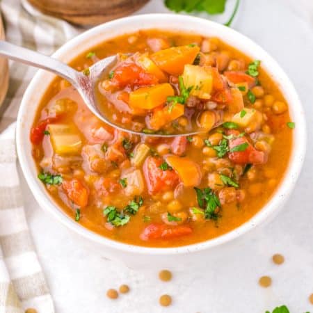 A soup spoon scooping up the Lentil Soup from a white bowl.