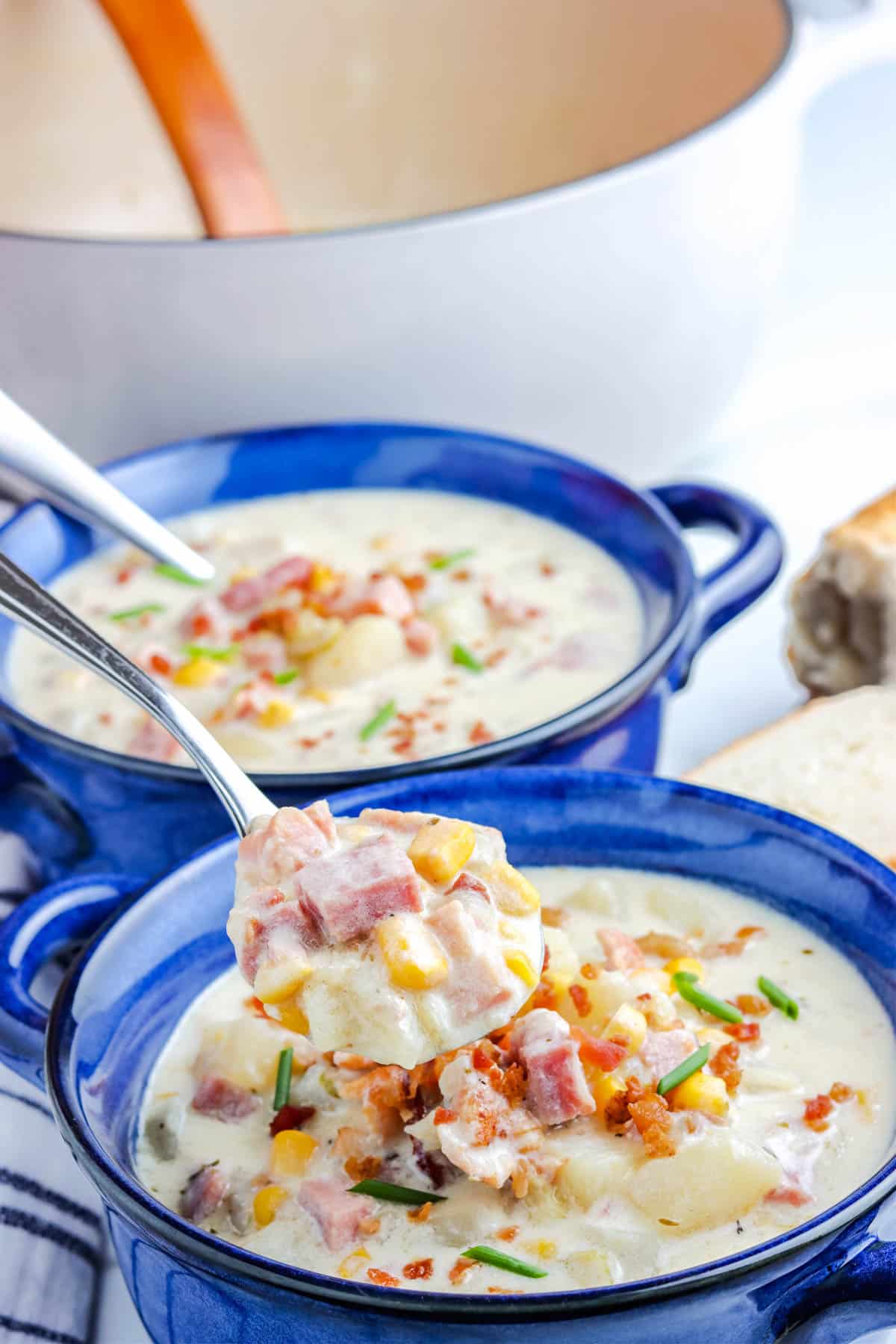 A spoon over a soup bowl with some of this corn chowder with ham and potatoes.