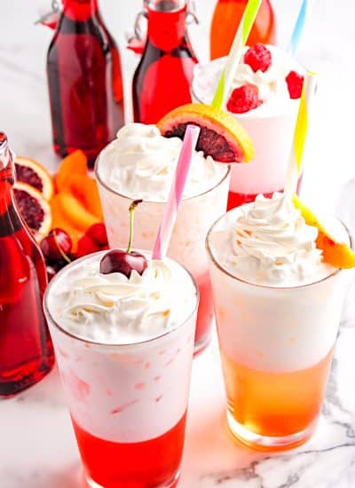 The finished Italian Cream Soda in clear glasses and garnished with whipped cream and fresh fruit.
