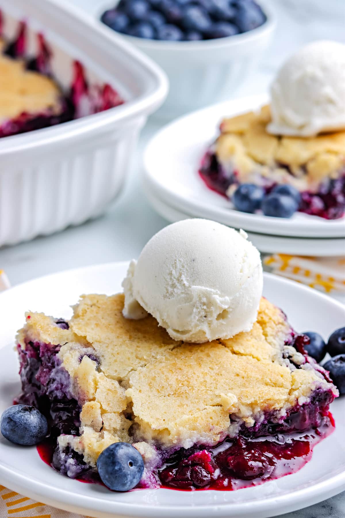 The finished Blueberry Cobbler on a white plate with a scoop of ice cream. 