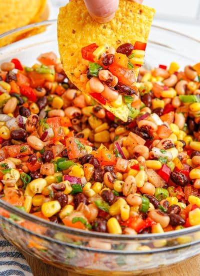 The finished Cowboy Caviar in a glass bowl and tortilla chip dipping into it.