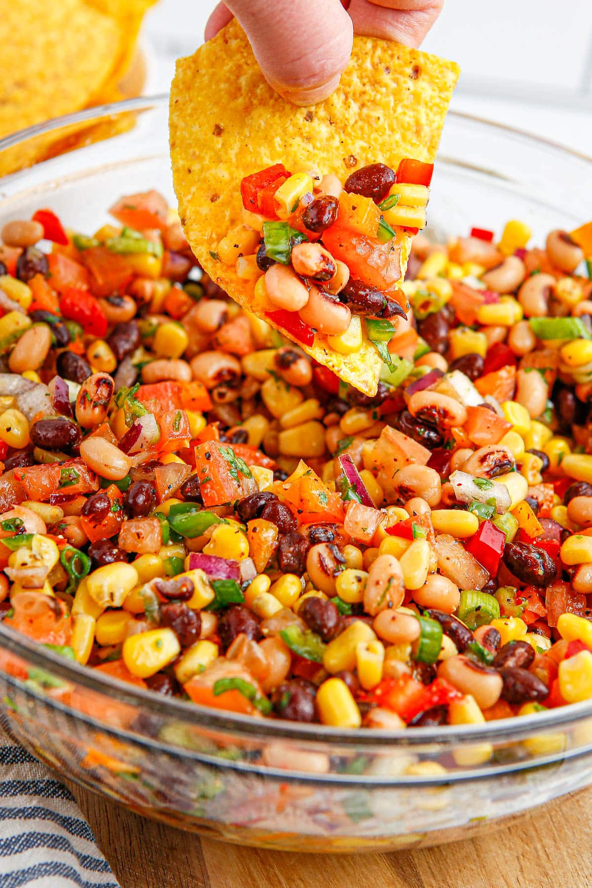 The finished Cowboy Caviar in a glass bowl and tortilla chip dipping into it. 