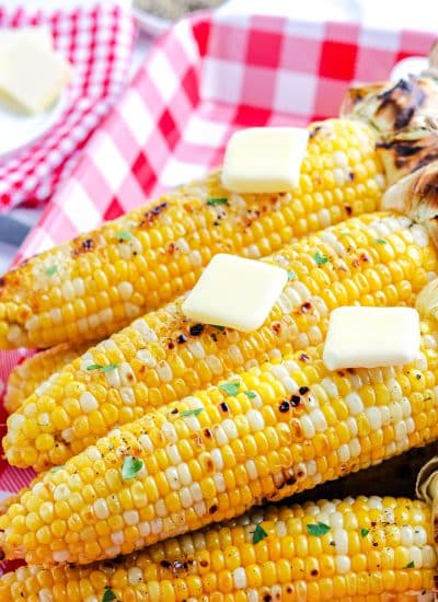 The finished grilled corn with the husk pulled back and topped with pads of butter.