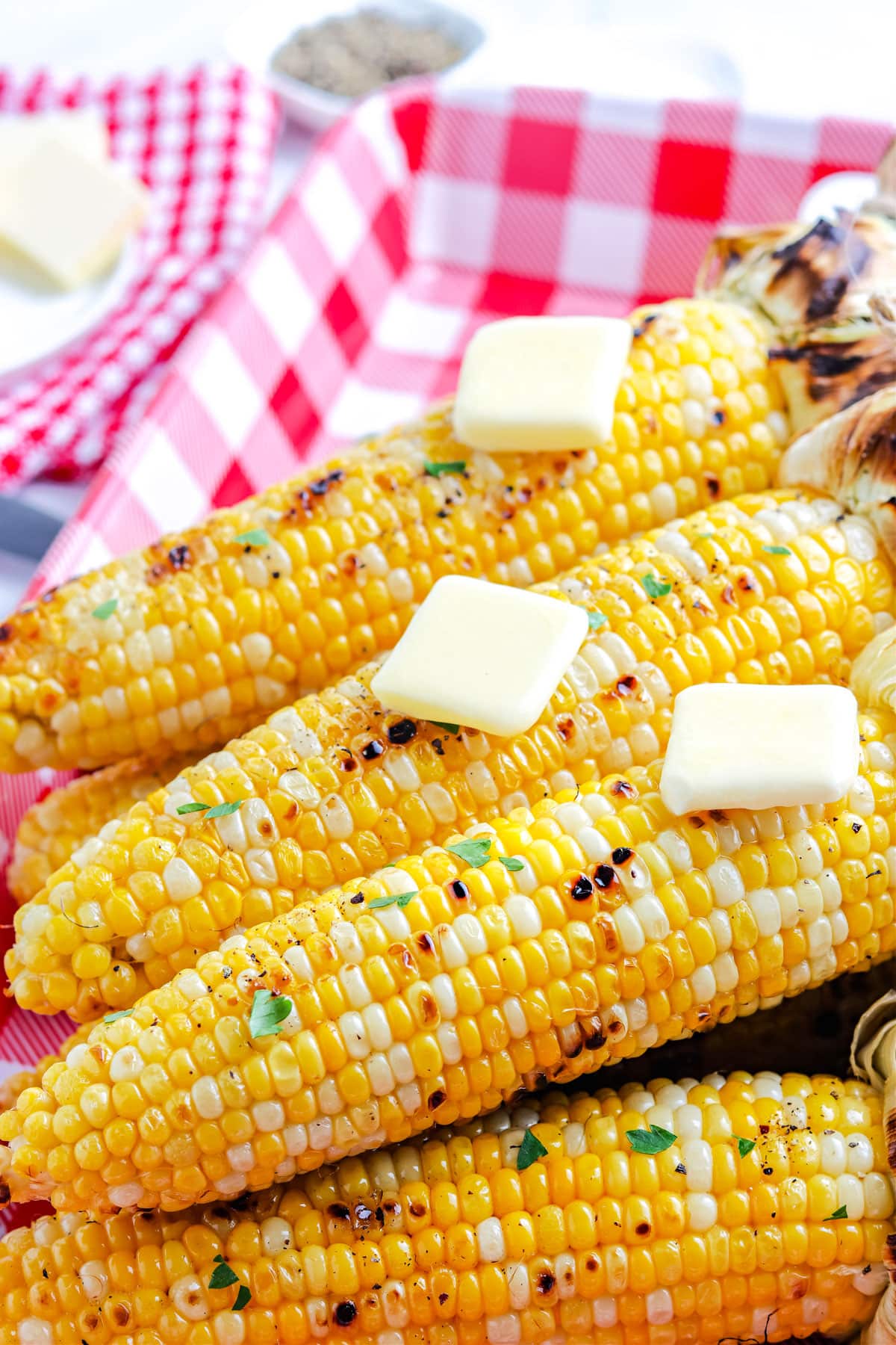 The finished grilled corn with the husk pulled back and topped with pads of butter.