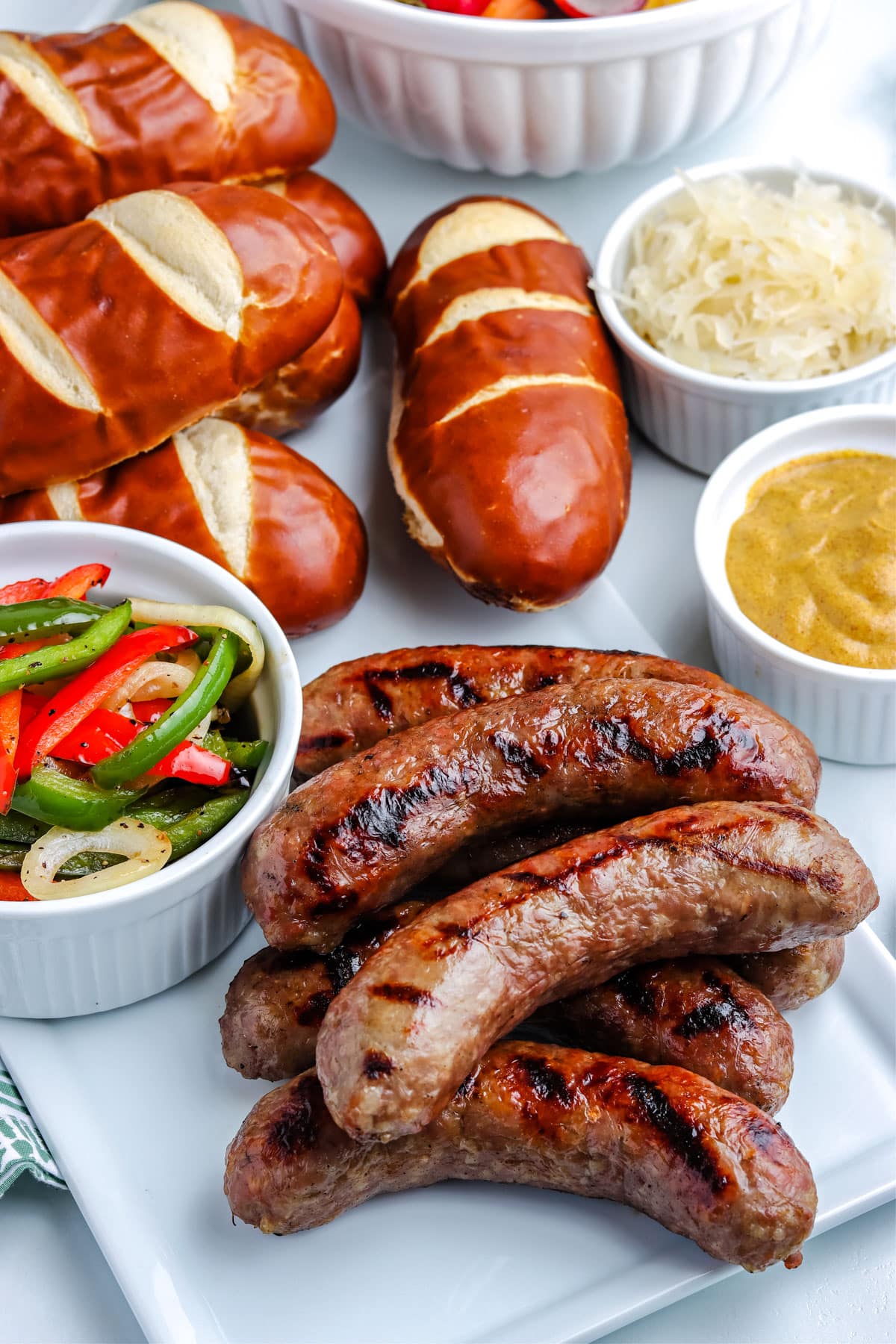 Finished Grilled Brats on a white serving platter with rolls in the background.