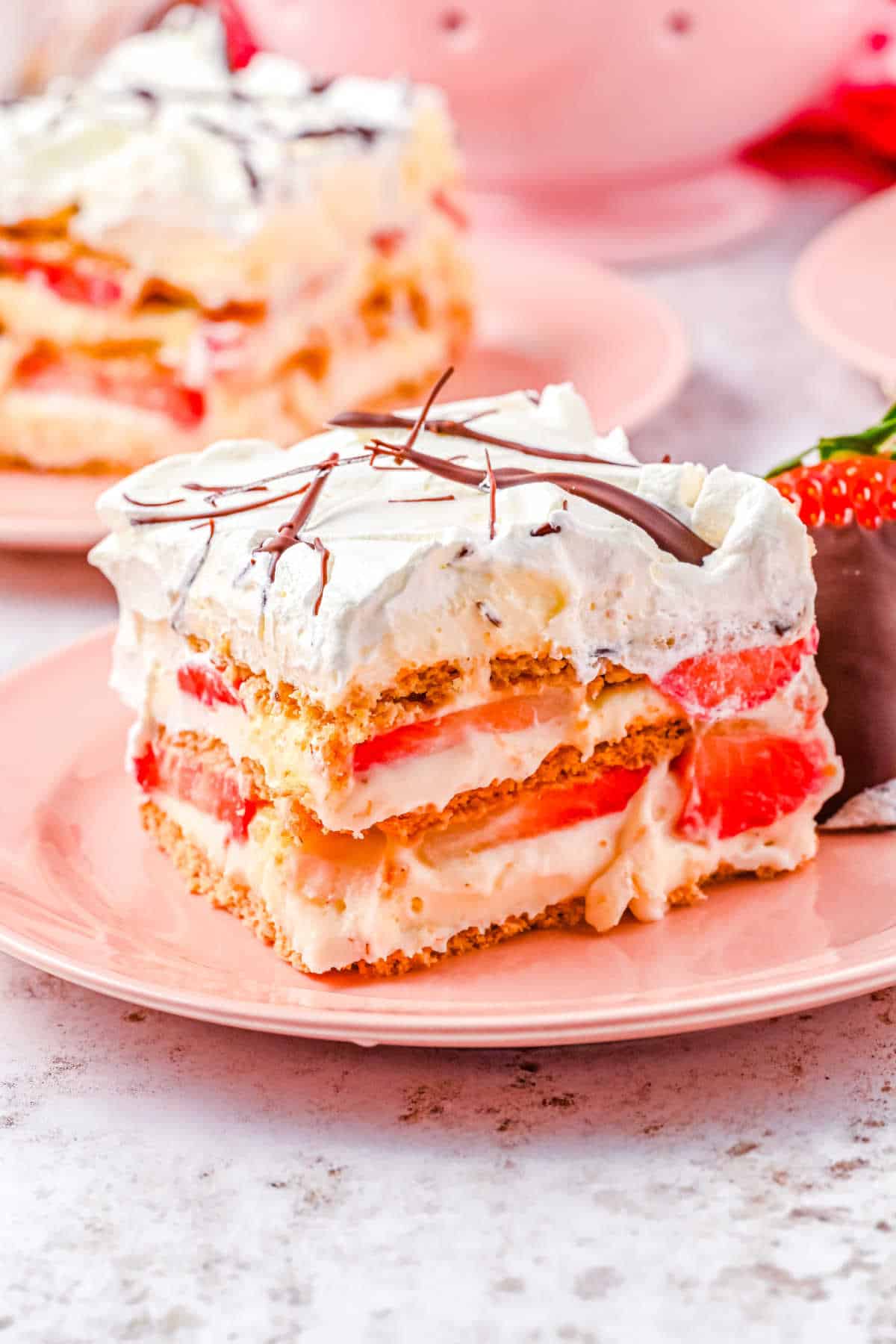 a slice of strawberry icebox cake on a pink plate with a chocolate covered strawberry on the side