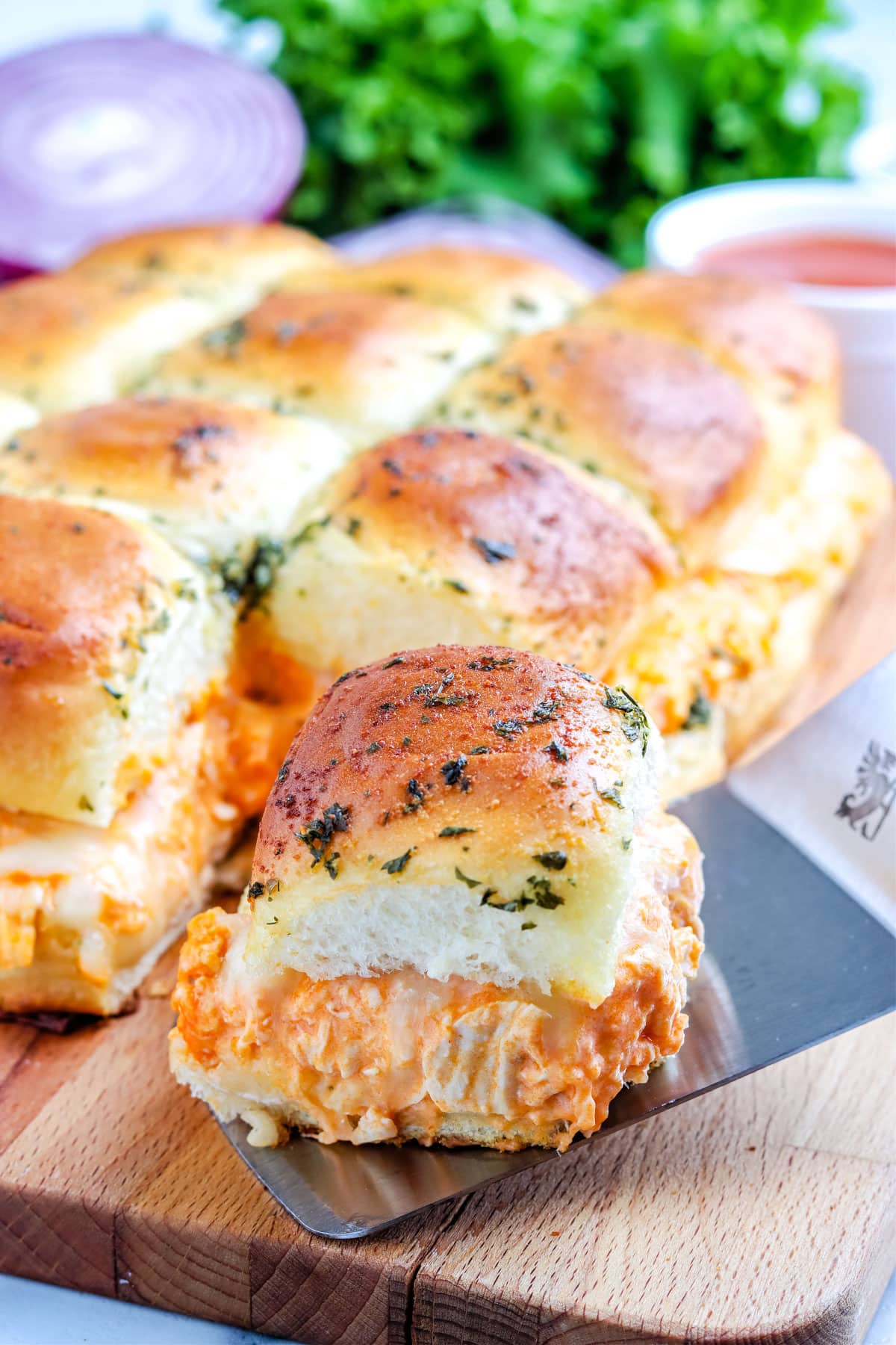 A spatula listing up a Buffalo Chicken Slider on Hawaiian Rolls.