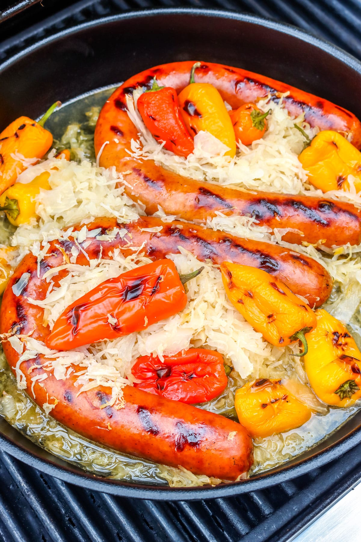 A pan full of kielbasa, sauerkraut, and peppers on a grill.