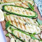 A close up of Grilled Zucchini strips on a wood cutting board.