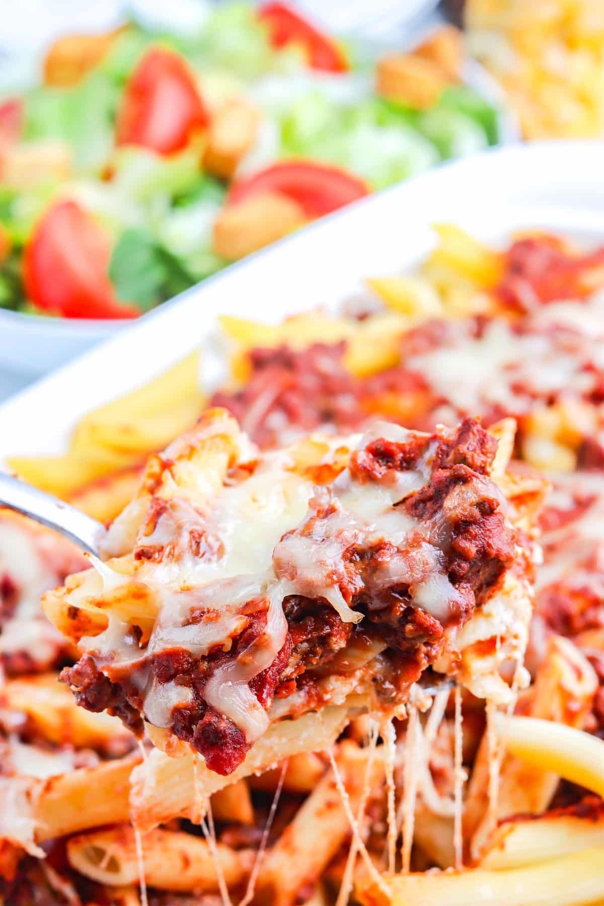 A serving spoon lifting up some of the baked penne pasta.