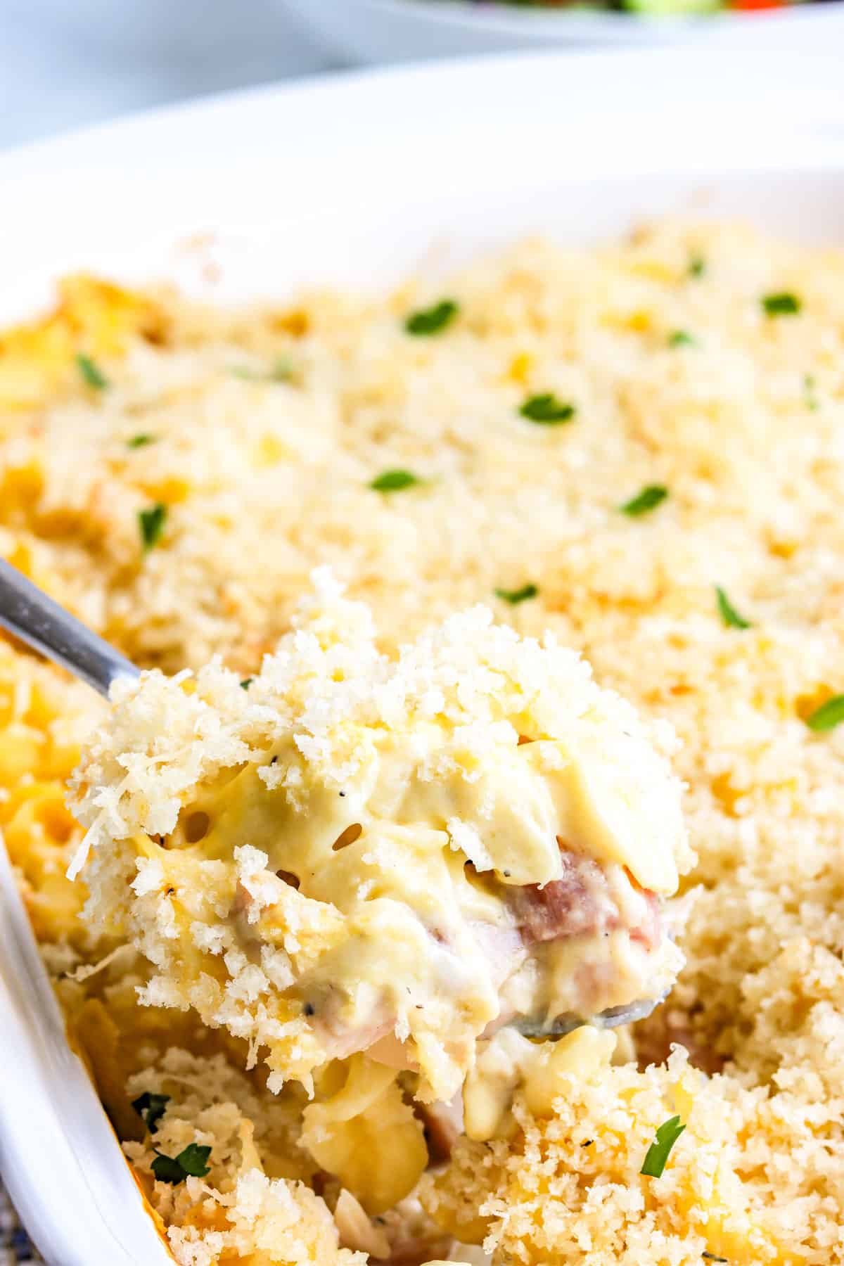 A spoon lifting some of the Chicken Cordon Bleu Casserole from the casserole dish. 