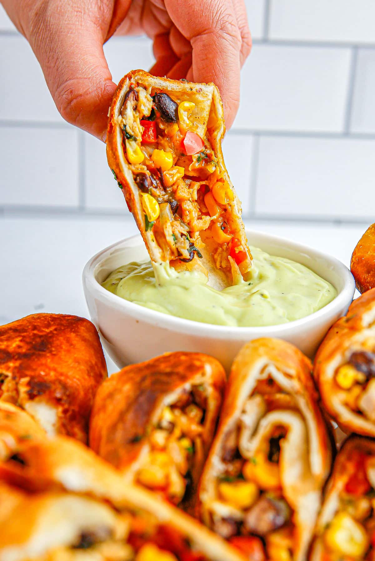 A Southwest Egg Roll being dipped into an avocado ranch sauce.