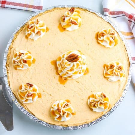 The finished no bake cream cheese pumpkin garnished with whipped cream, caramel, and pecans.