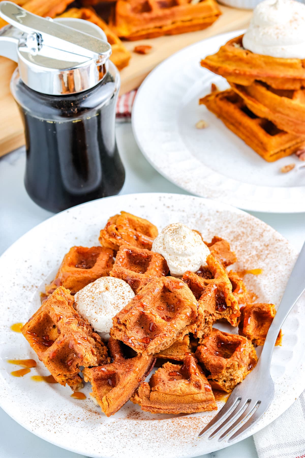 The finished Pumpkin Waffles recipe on a white plate and topped with whipped cream and syrup.