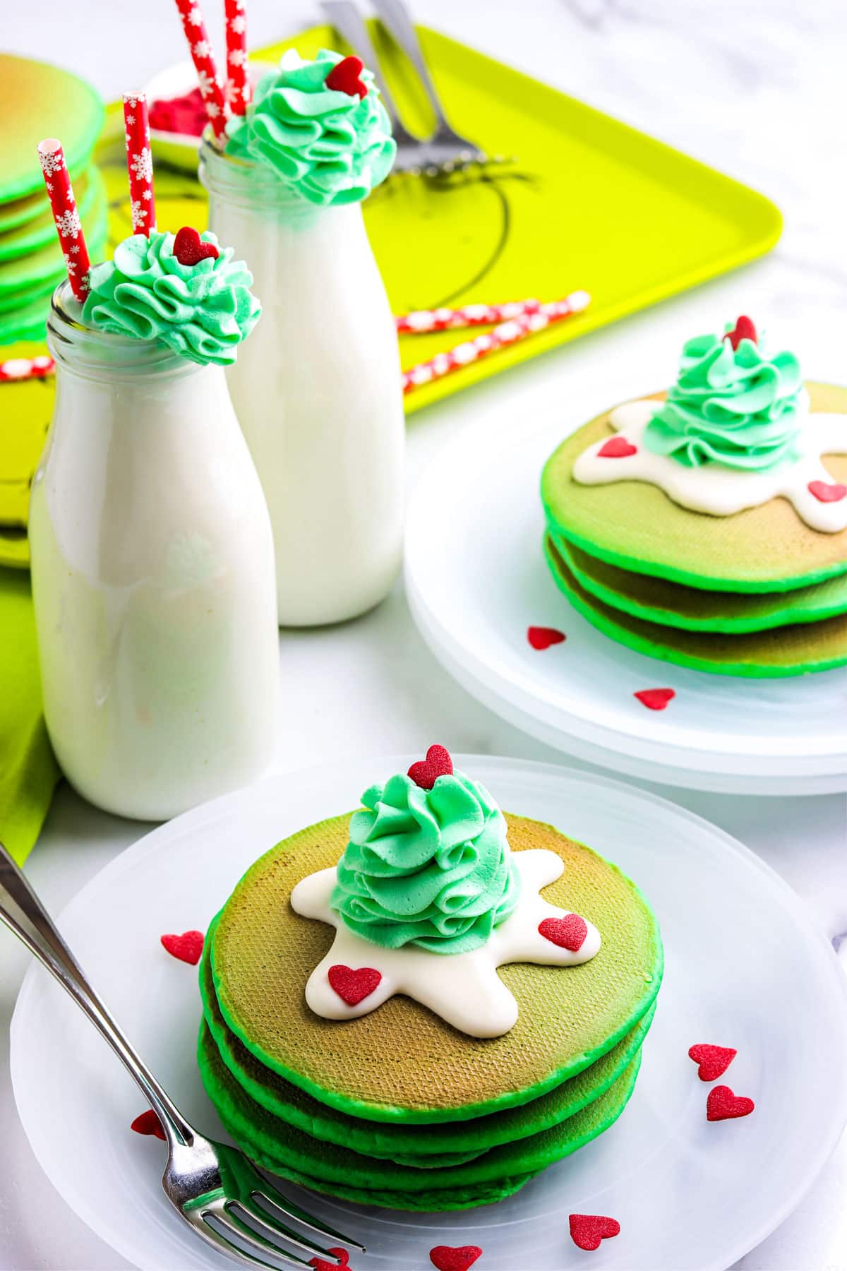 Stacks of Grinch Pancakes bon white plates and garnished with green whipped cream and red heard sprinkles.