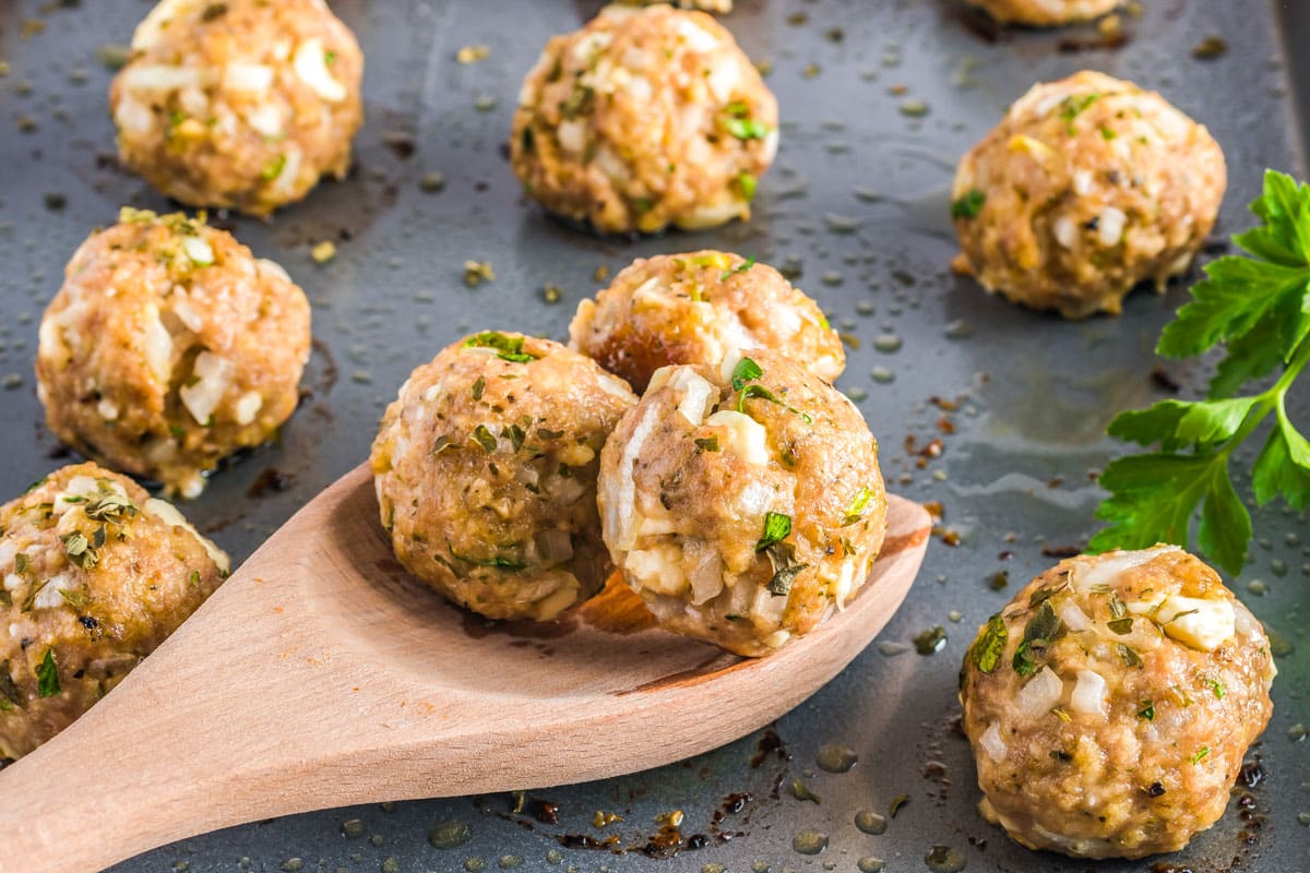 A spoon picking up some Turkey Feta Meatballs from a baking sheet.