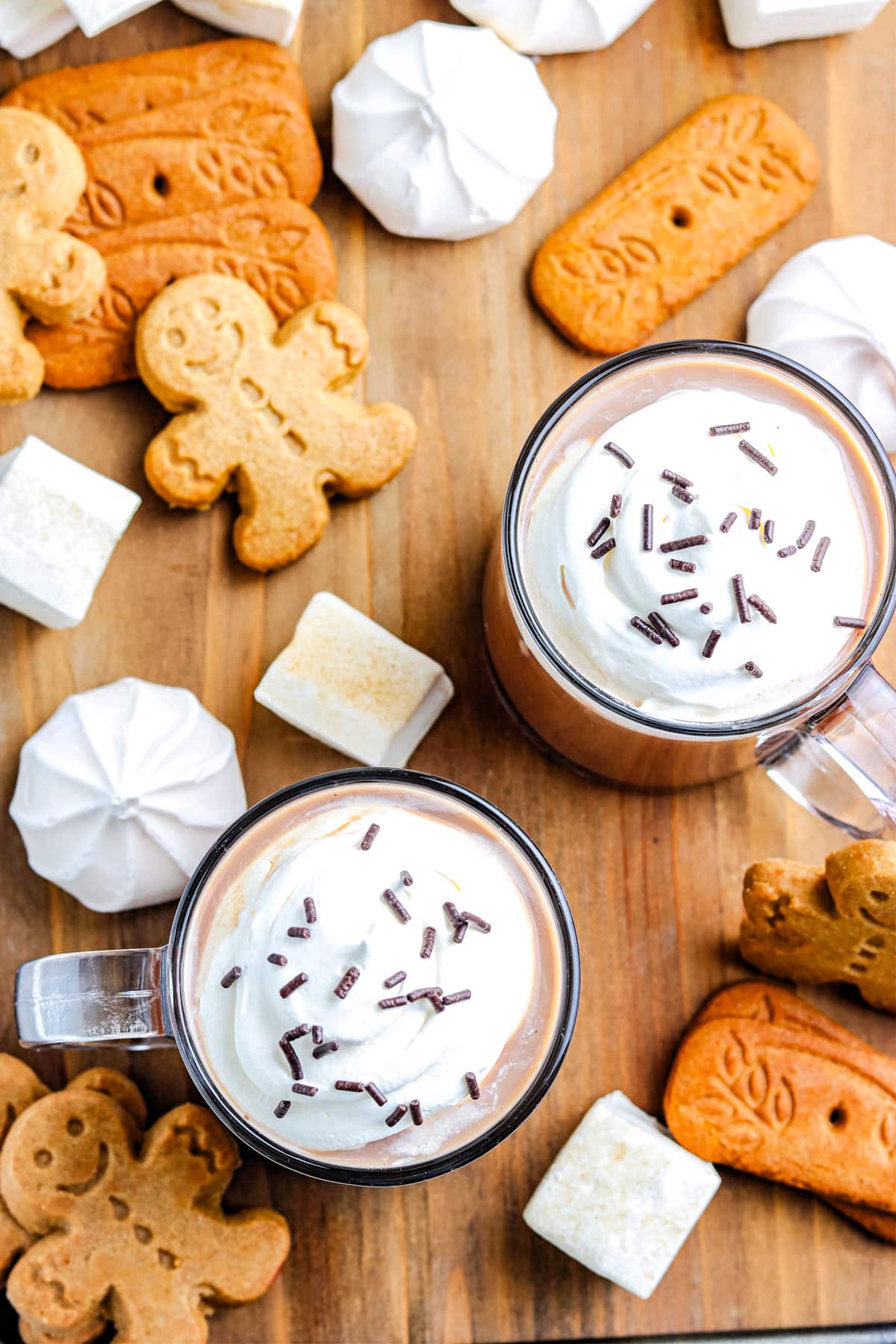 An overhead picture of two mugs of the finished Gingerbread Hot Chocolate recipe with marshmallows, gingerbread cookies, and meringue cookies.