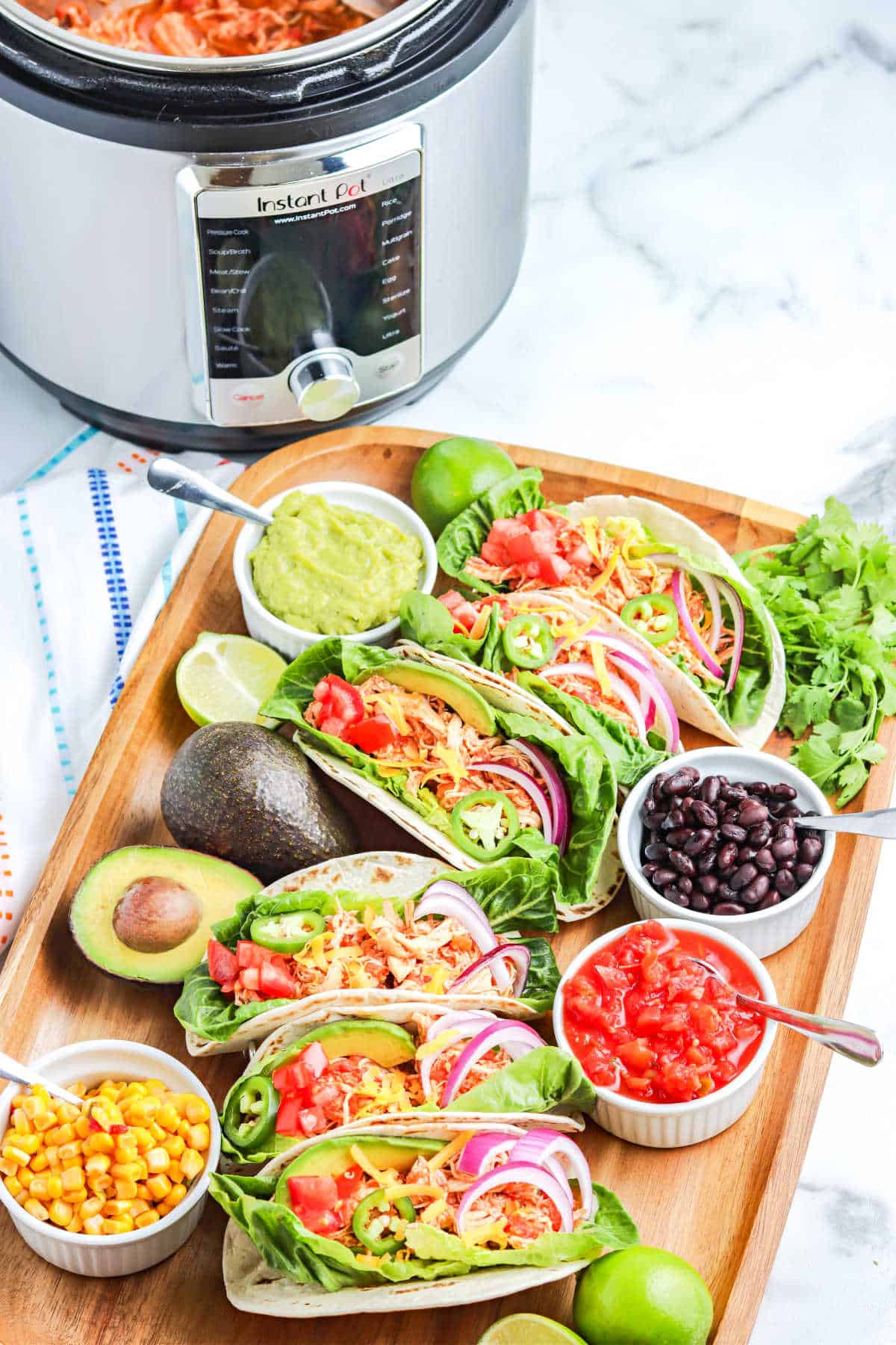 instant pot salsa chicken being used for serving in tacos with toppings on a cutting board and an instant pot in the background