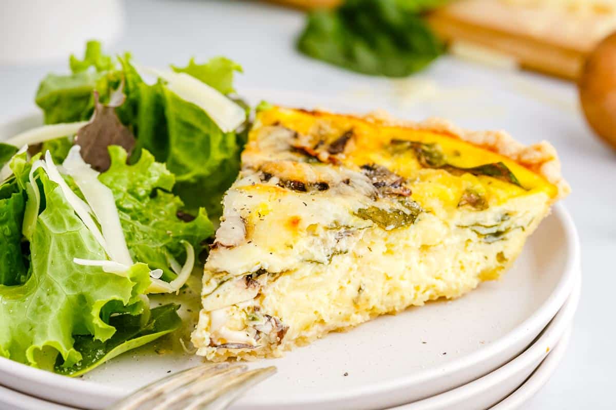 A close up picture of a slice of mushroom and spinach quiche.