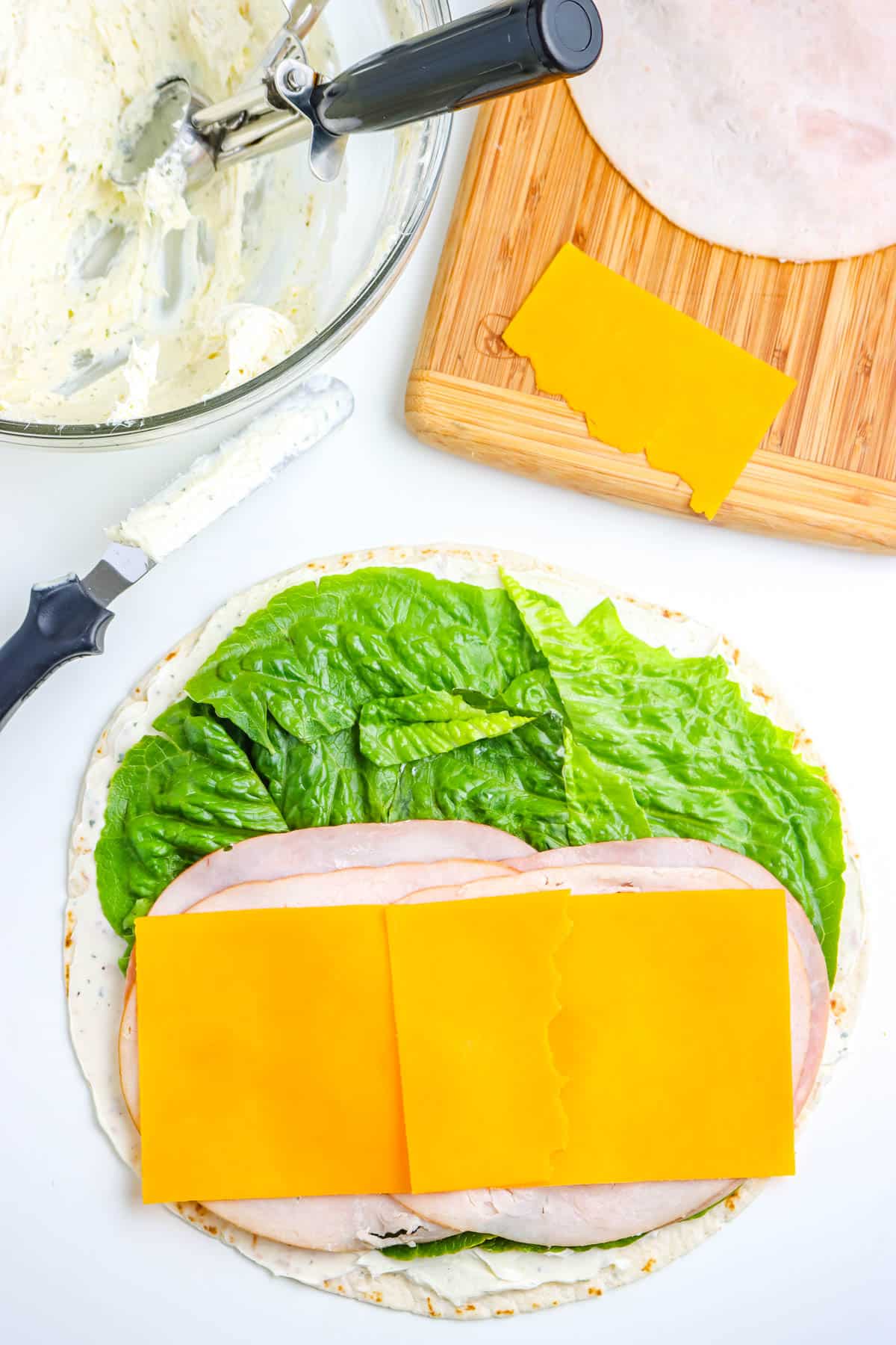 The spread, lettuce, meat, and cheese on tortilla.