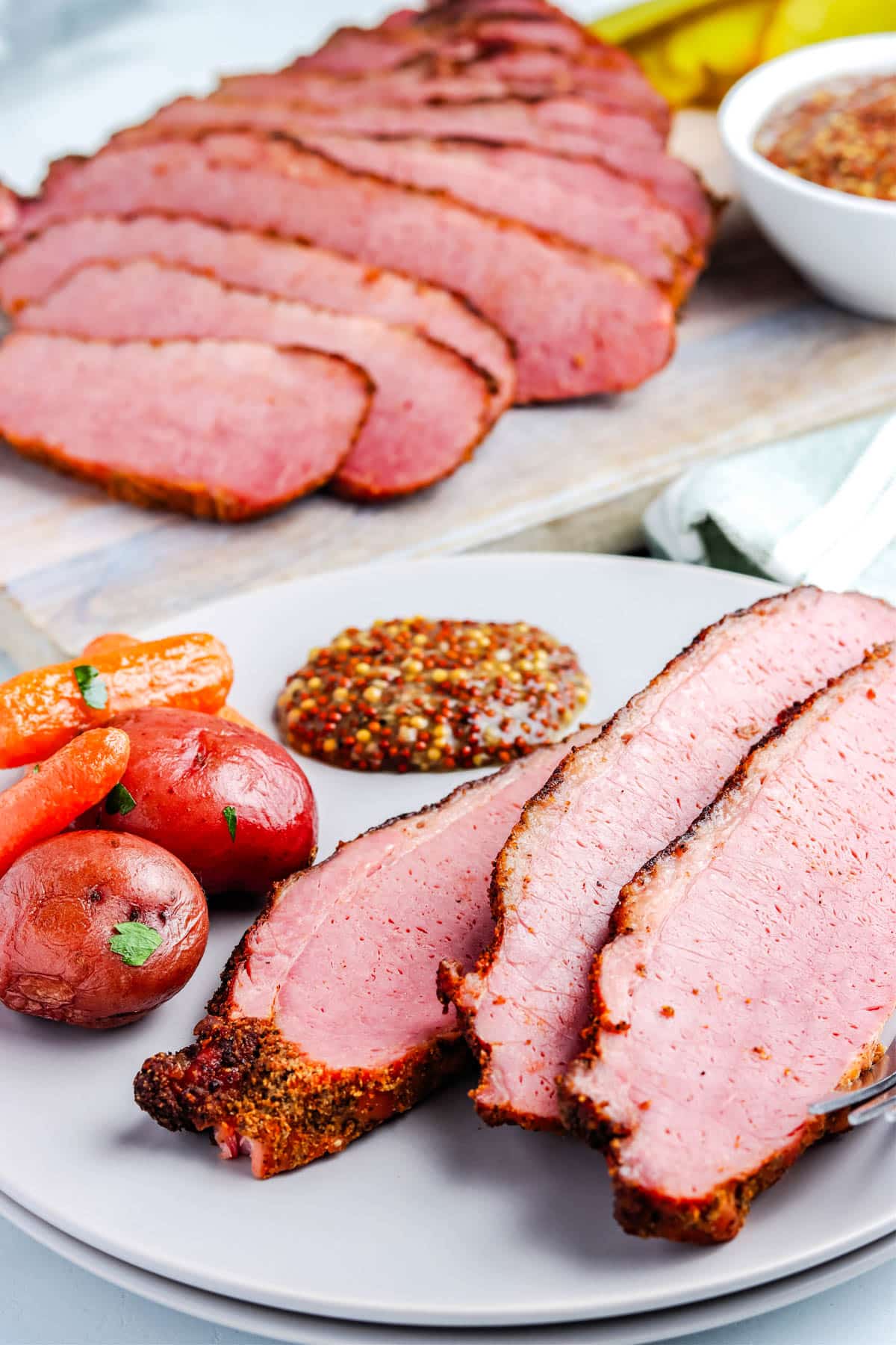 Three slices of Smoked Corned Beef Brisket on a plate with potatoes and grainy mustard.