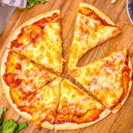 A tortilla pizza on a cutting blade cut into slices.