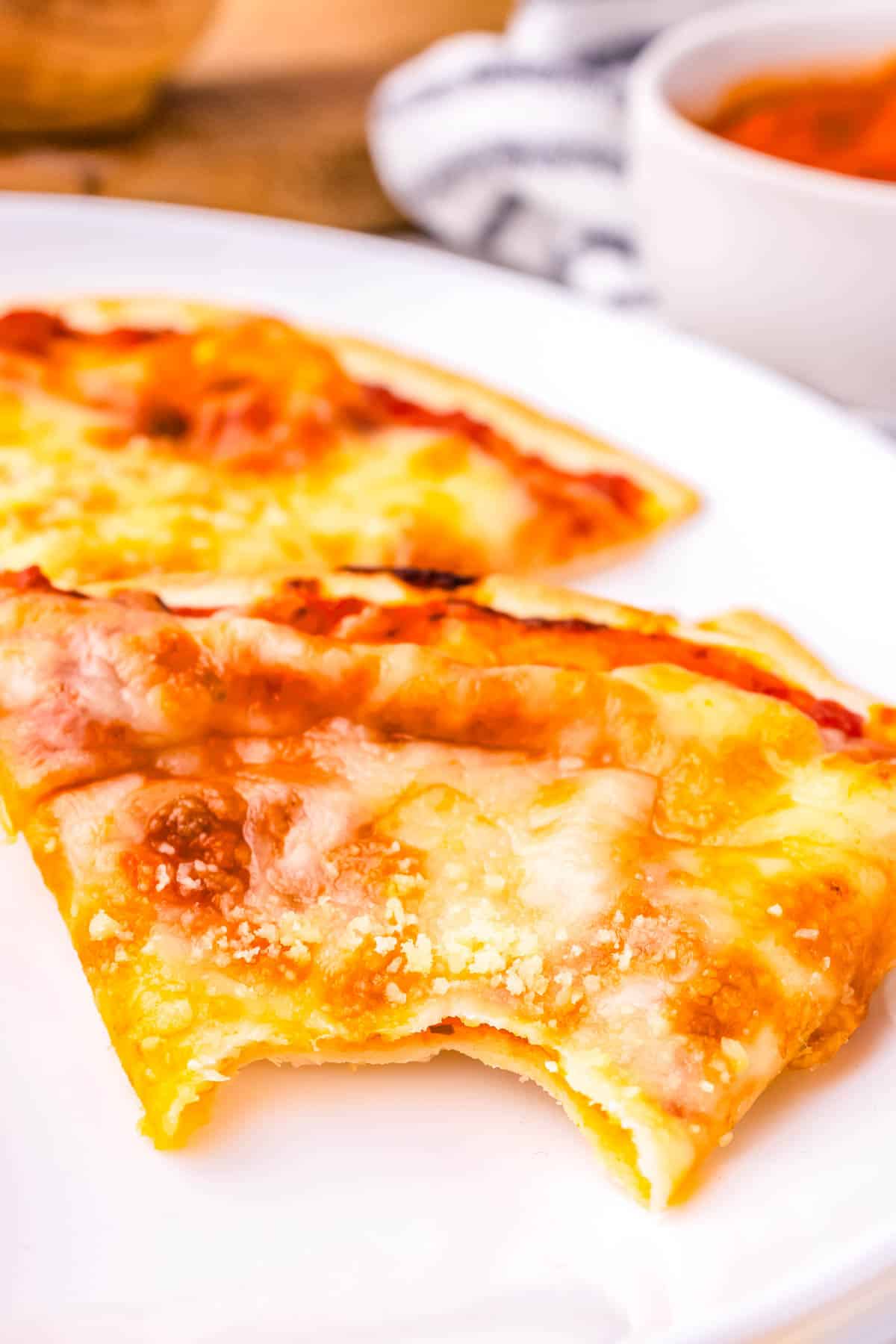 Two slices of tortilla pizza on a plate, one with a bite taken out of it.